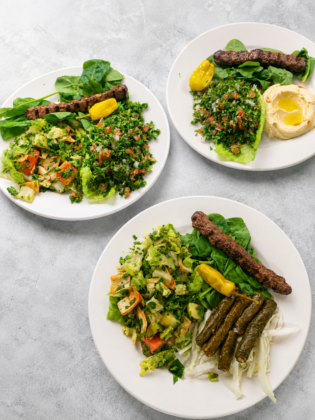 Three plates of Lebanese dishes – kafta kebab, tabbouleh, hummus and grape leaves